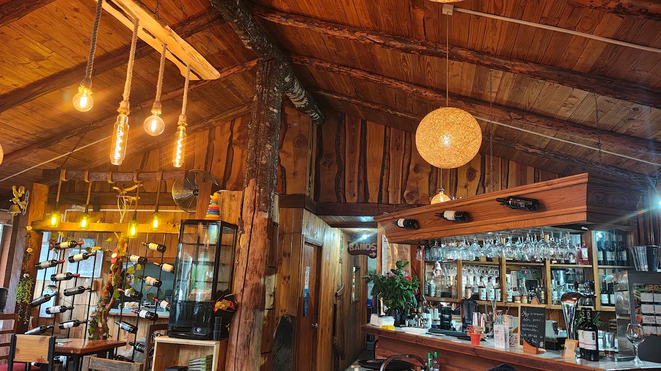 Comedor de Adkantú de noche: techo de madera, lámparas colgantes y la barra al fondo.