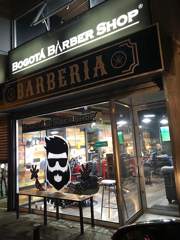 Fachada de Bogotá Barber Shop de noche, con el letrero iluminado y el logo en la vitrina