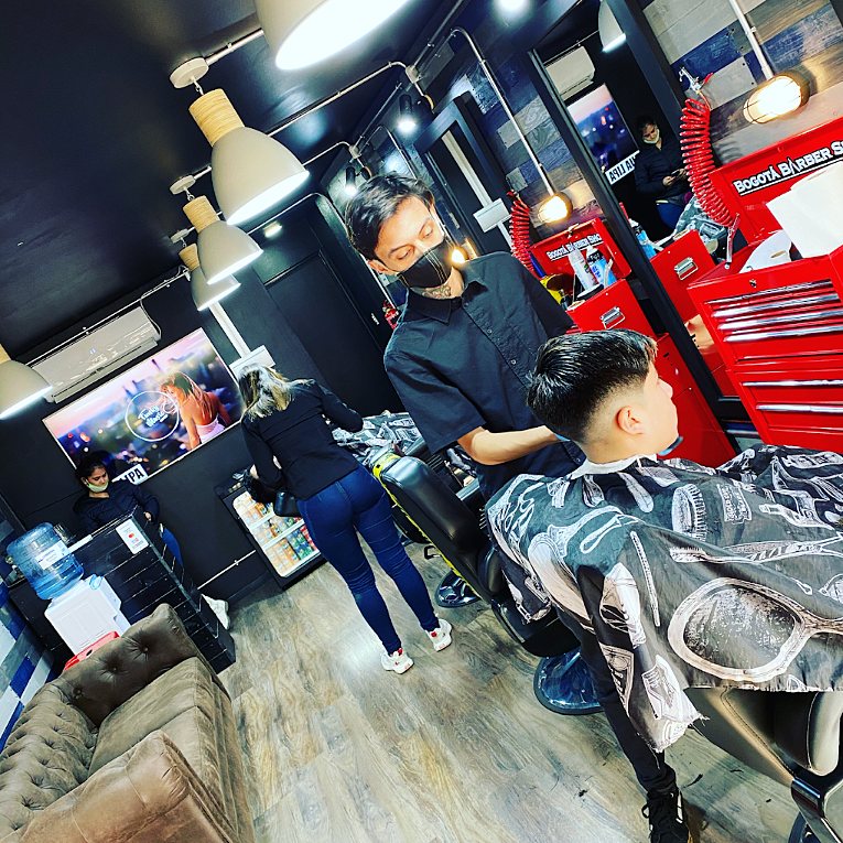 Barbero cortando el pelo a un cliente, con los muebles de herramientas rojos de la barbería al fondo