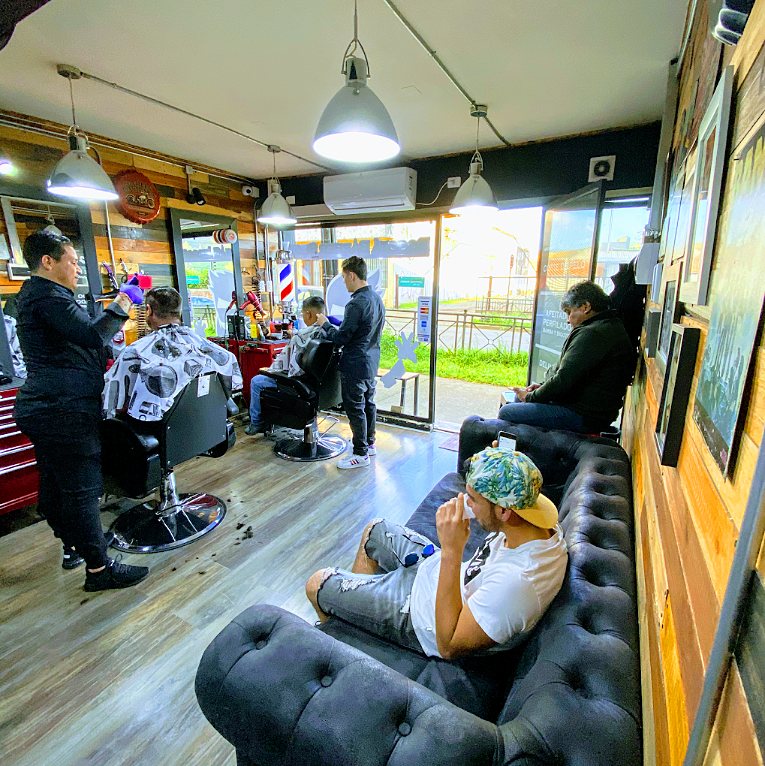 Zona de espera con sofá de cuero y clientes sentados, con los sillones de corte al fondo