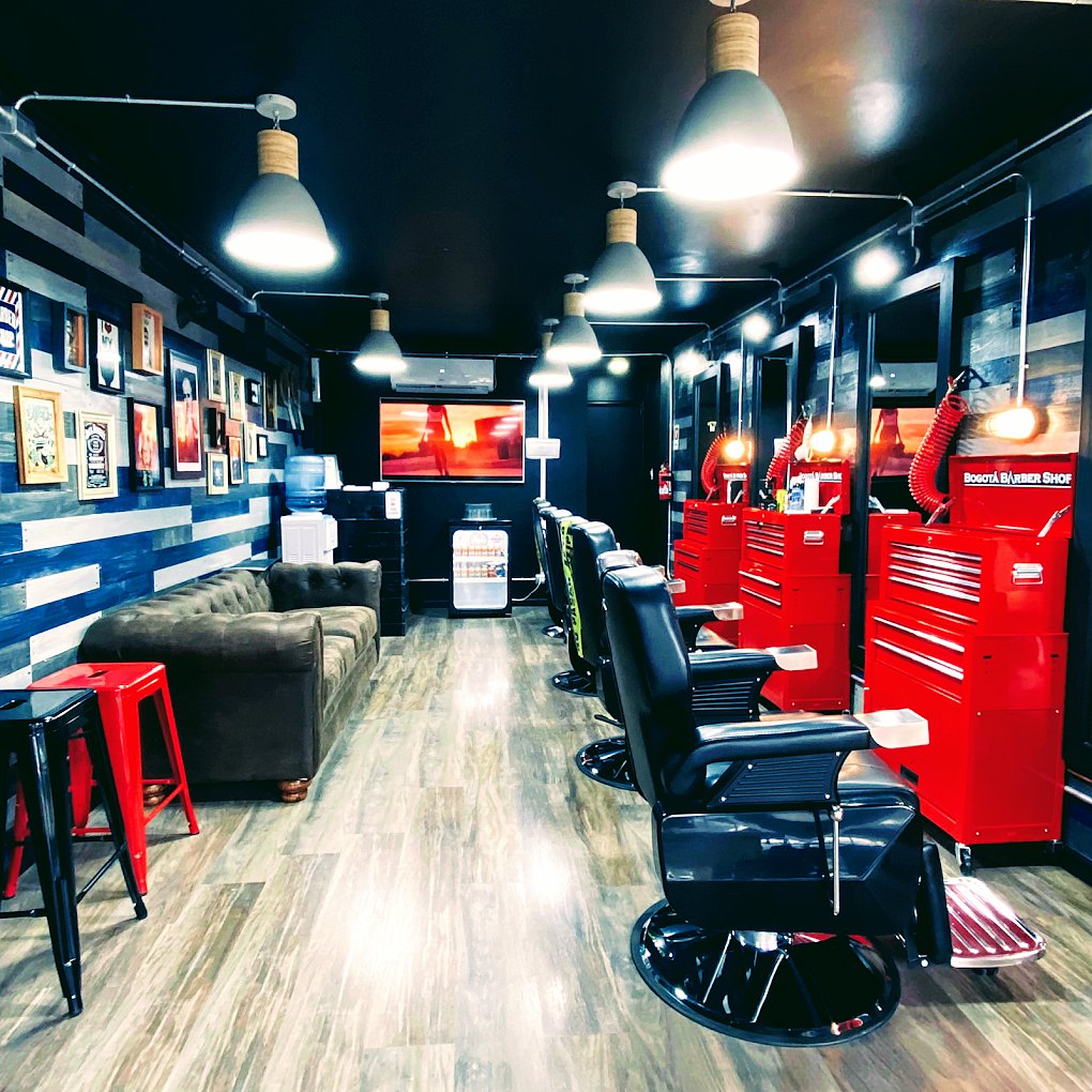 Interior de Bogotá Barber Shop: fila de sillones de barbero negros frente a los muebles de herramientas rojos, con lámparas colgantes y un sofá de espera