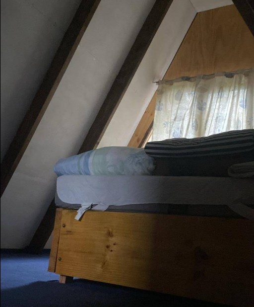 Dormitorio en el altillo, con el techo inclinado de la cabaña bajando sobre la cama.