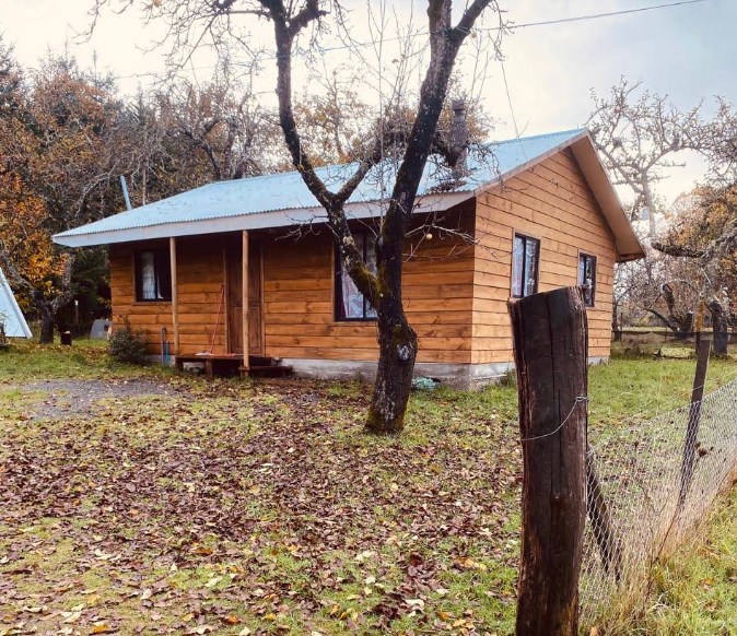 La segunda casa de madera del campo en otoño, rodeada de hojas caídas y árboles frutales.