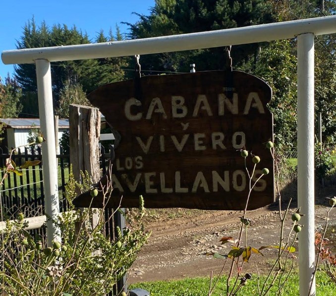 Letrero de madera pintado a mano que dice Cabaña y Vivero Los Avellanos, colgado en el acceso.