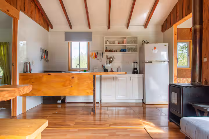 Cocina de la cabaña con muebles blancos y mesón de madera