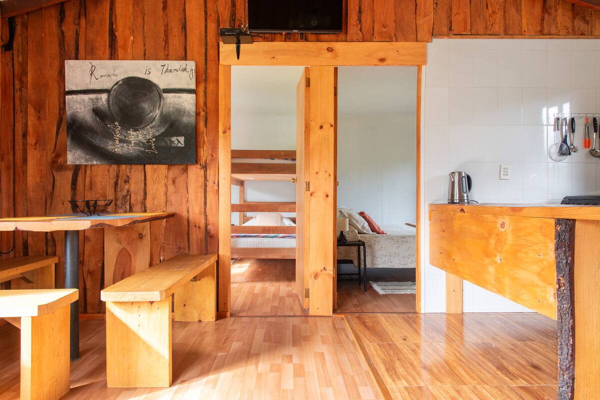 Comedor de la cabaña con mesa alta de madera y escalera al altillo