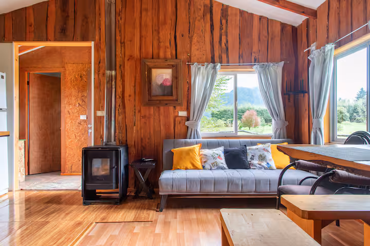 Living con estufa a leña, sofá y mesa de madera