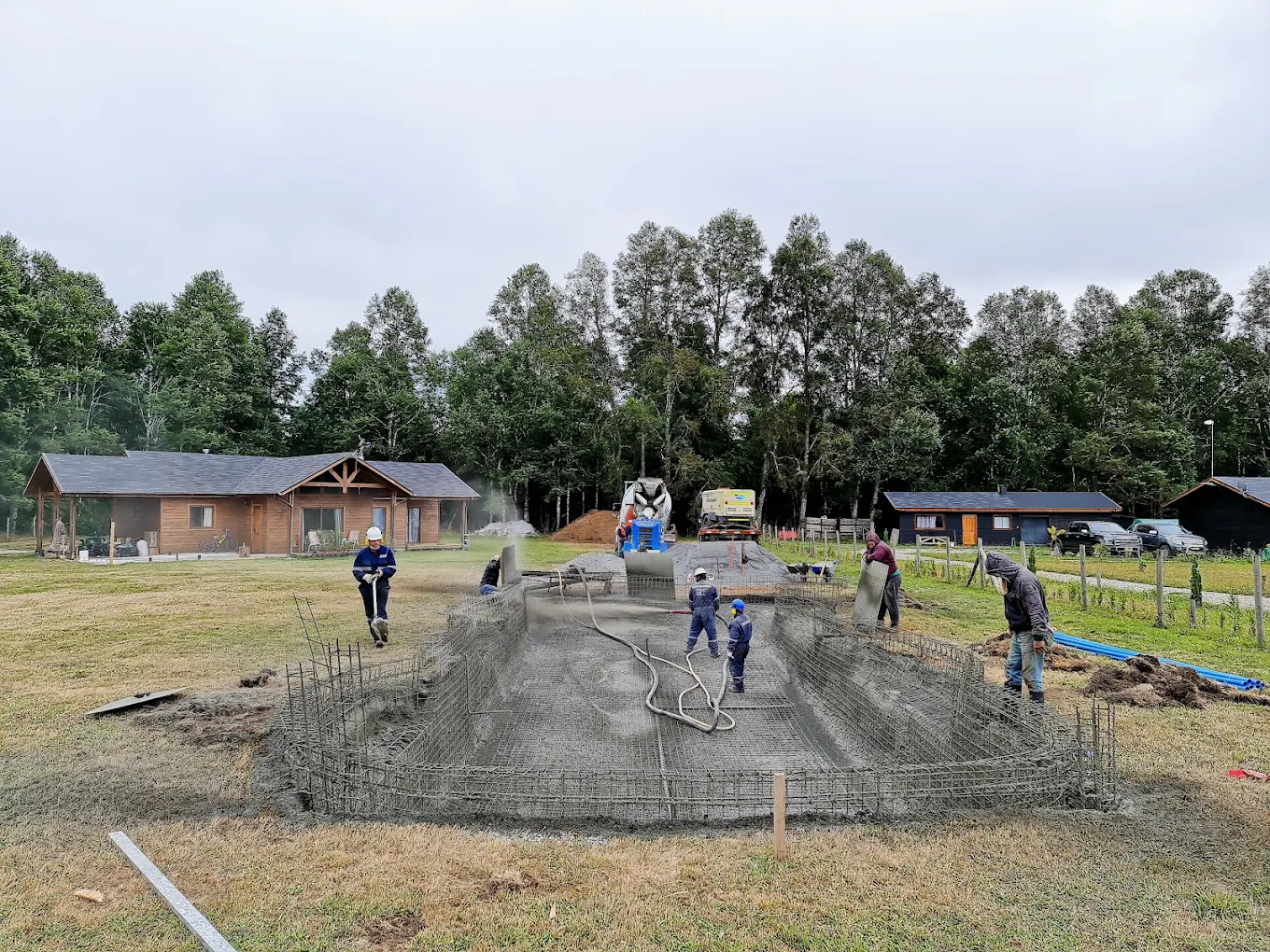 Cuadrilla de ekla vaciando y reglando el hormigón de una fundación corrida, con bosque al fondo.