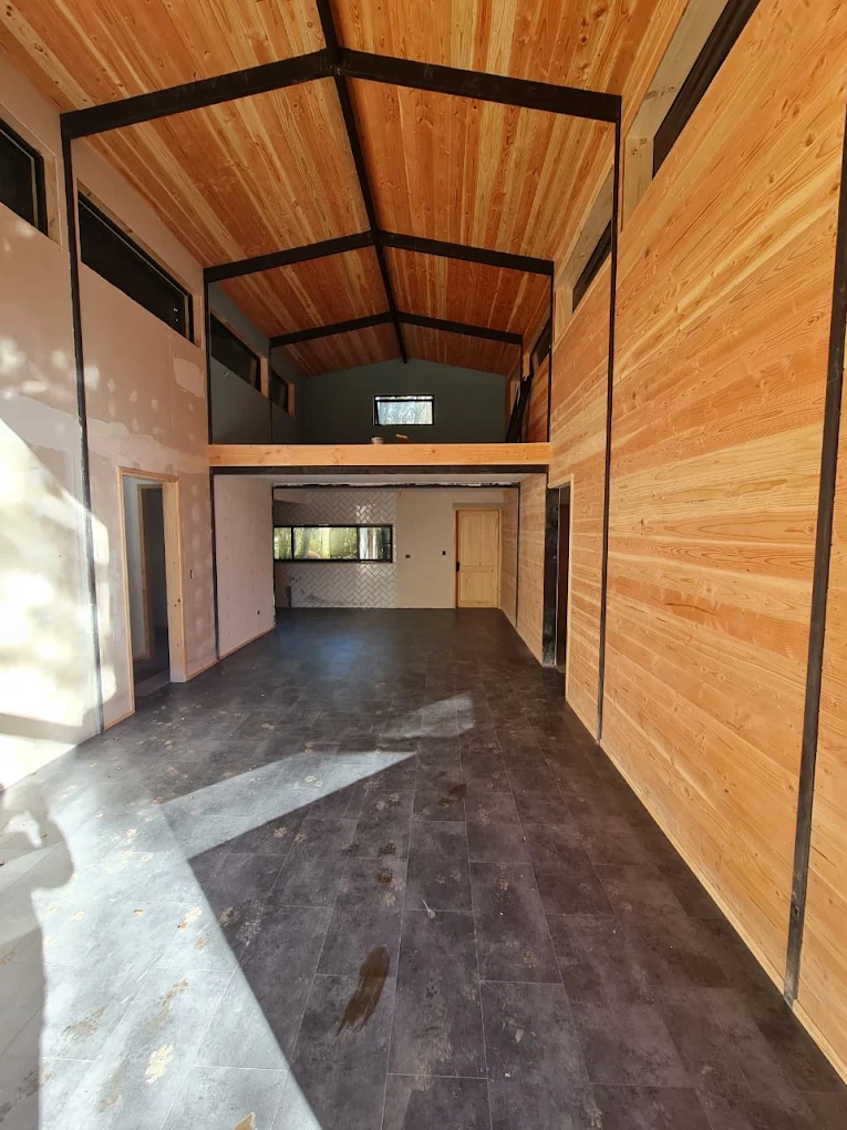 Interior de un galpón revestido íntegramente en madera, con radier pulido y portón abierto.