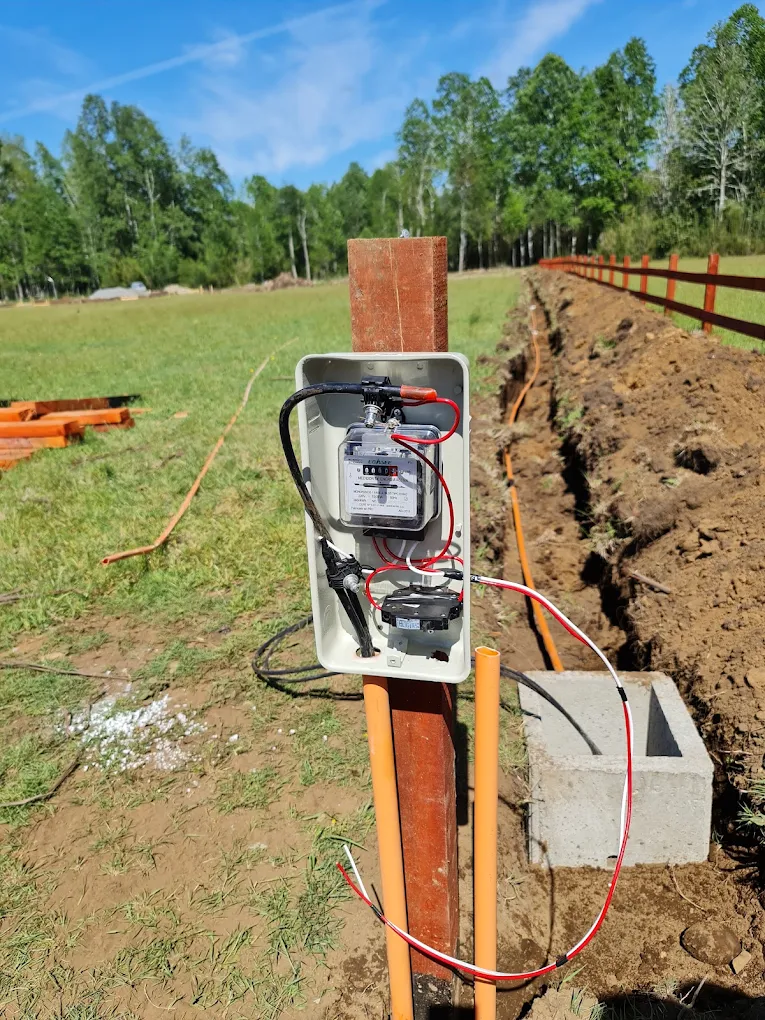 Empalme eléctrico montado en un poste de madera junto a una zanja abierta para la canalización.