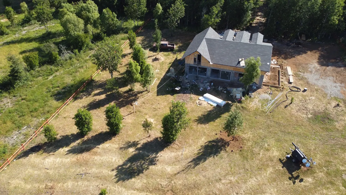 Vista aérea de una casa grande en construcción emplazada en una ladera con árboles jóvenes alrededor.