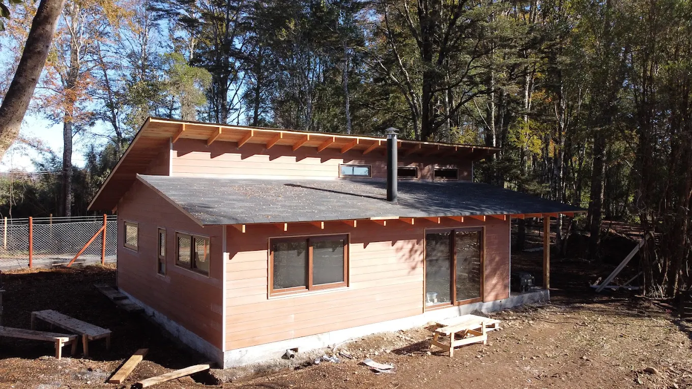 Casa en obra gruesa con revestimiento de madera y techumbre puesta, en un terreno arbolado.