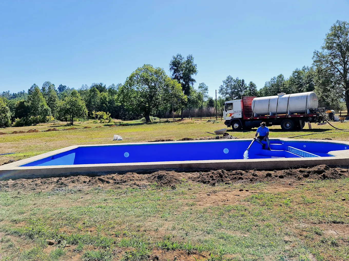 Piscina de hormigón recién revestida en azul, llenándose con un camión aljibe estacionado al costado.
