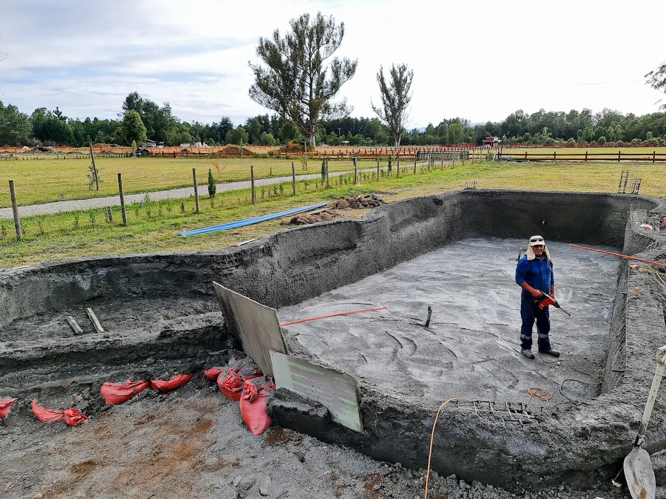 Excavación de una piscina con moldaje metálico armado y un trabajador con casco dentro del vaso.