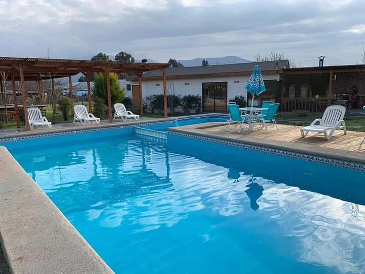 Piscina en uso con solárium, reposeras y quincho techado al fondo en un día despejado.
