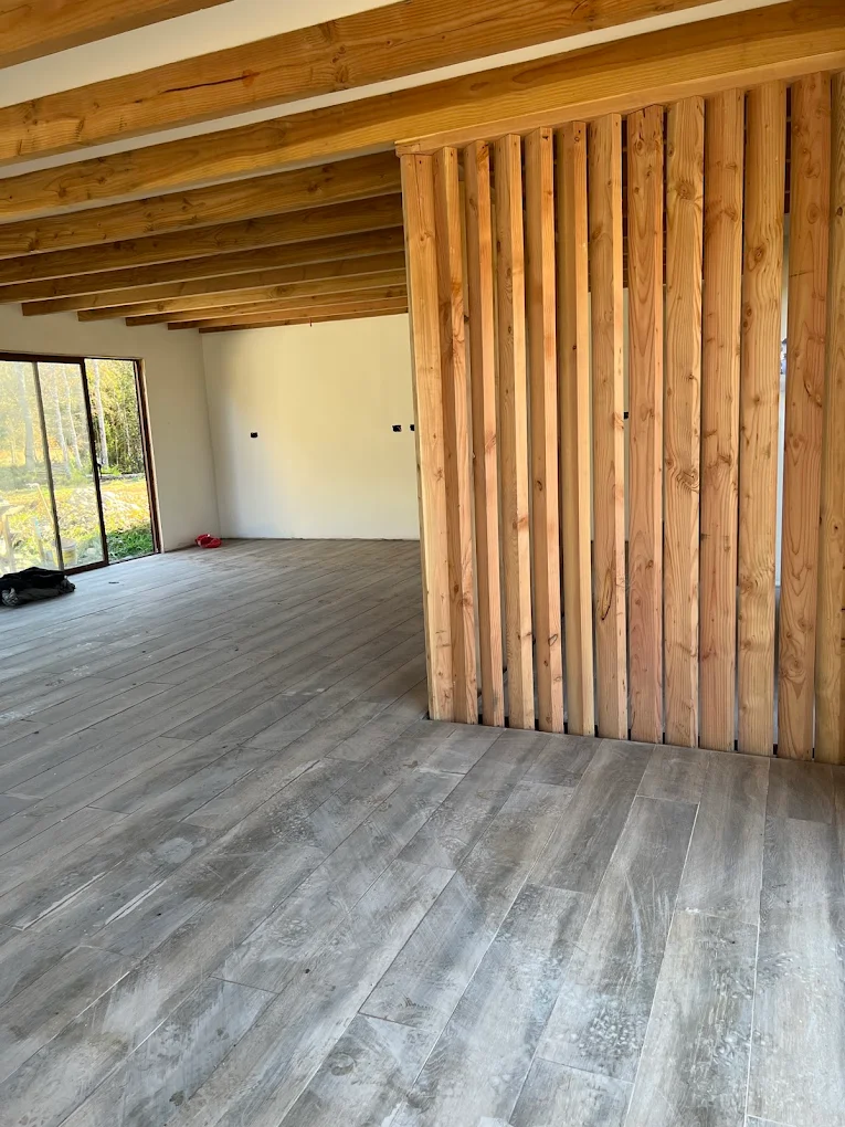 Interior terminado con tabique de listones de madera, viga a la vista y piso flotante recién puesto.