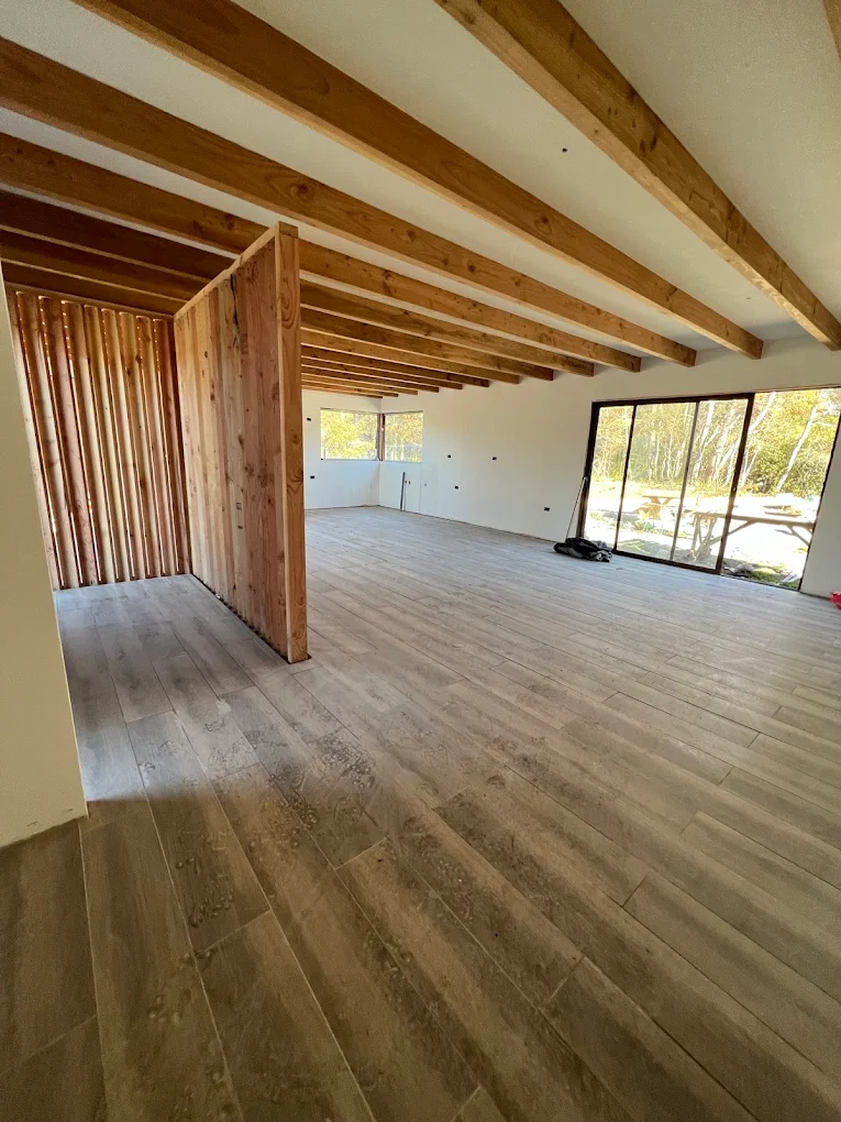 Interior con piso flotante recién instalado, vigas de madera a la vista y ventanal al jardín.