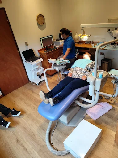 Atención en curso en el box de la clínica: la paciente en el sillón y el dentista trabajando con el instrumental a mano.