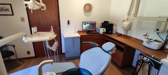 Vista completa de un box de la clínica con sillón dental, lámpara, mueble de instrumental y pantalla de radiografías.