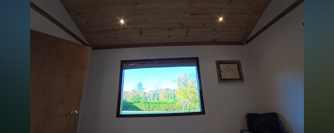 Interior del box con techo de madera y una ventana que da al bosque, con el título profesional colgado en la pared.
