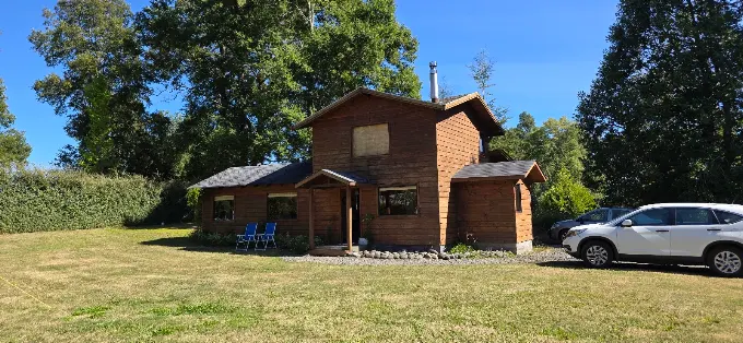 La casa de dos pisos de madera donde funciona la clínica, con pasto verde y cielo despejado.