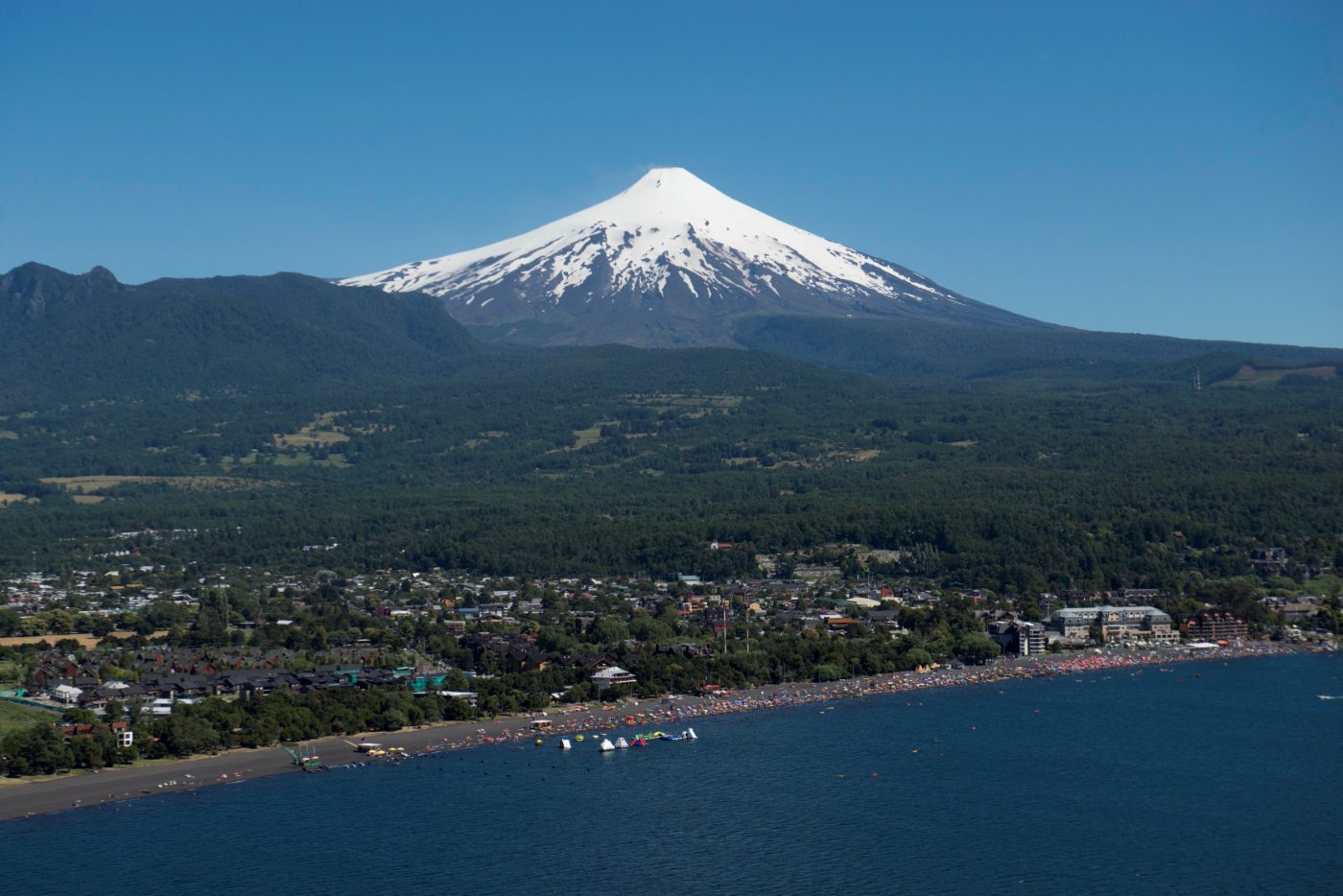 Vista aérea de Pucón: el pueblo y la playa del lago Villarrica con el volcán nevado detrás.