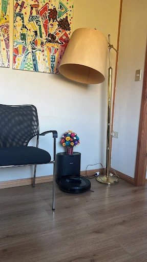 Rincón de la sala de espera con piso de madera, una silla, una lámpara de pie y un cuadro de colores.