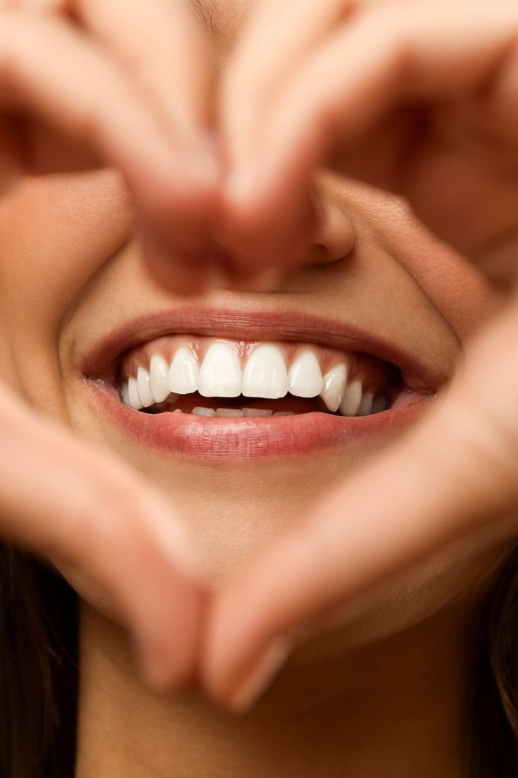Una mujer sonriendo enmarca su sonrisa con las manos formando un corazón.
