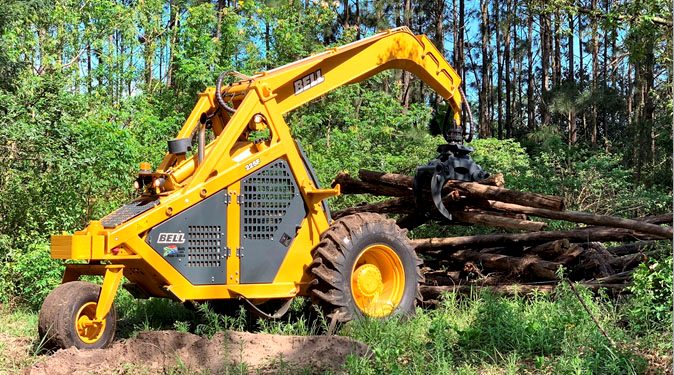 Bell trineumático, logger de tres ruedas con grúa y garra, junto a fustes apilados