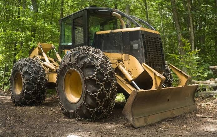 Skidder forestal con cadenas en las ruedas y hoja empujadora delantera, en el bosque