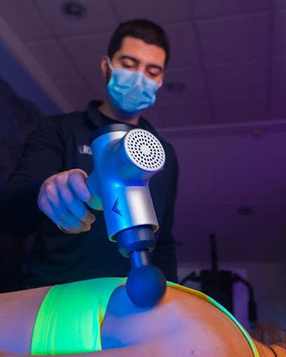 Kinesiólogo aplicando una pistola de percusión sobre la pierna de un paciente.