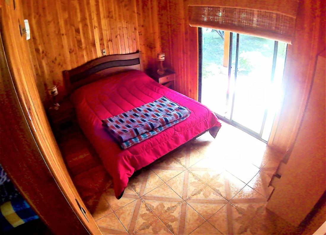 Dormitorio con cama de dos plazas, revestimiento de madera y una puerta ventana que da al jardín.