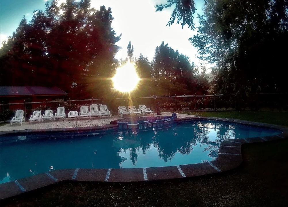 La piscina exterior al atardecer, con el sol entre los árboles y las tumbonas en la terraza de madera.