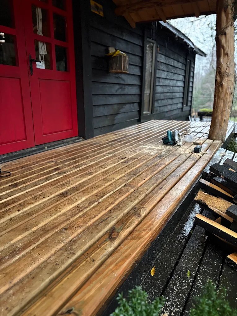 Deck de madera recién construido junto a una casa negra con puerta roja.