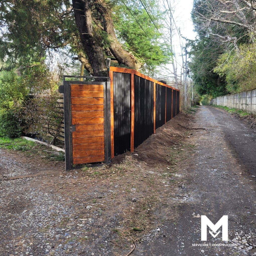 Portón y cerco perimetral de madera y fierro cerrando un callejón de acceso entre árboles.