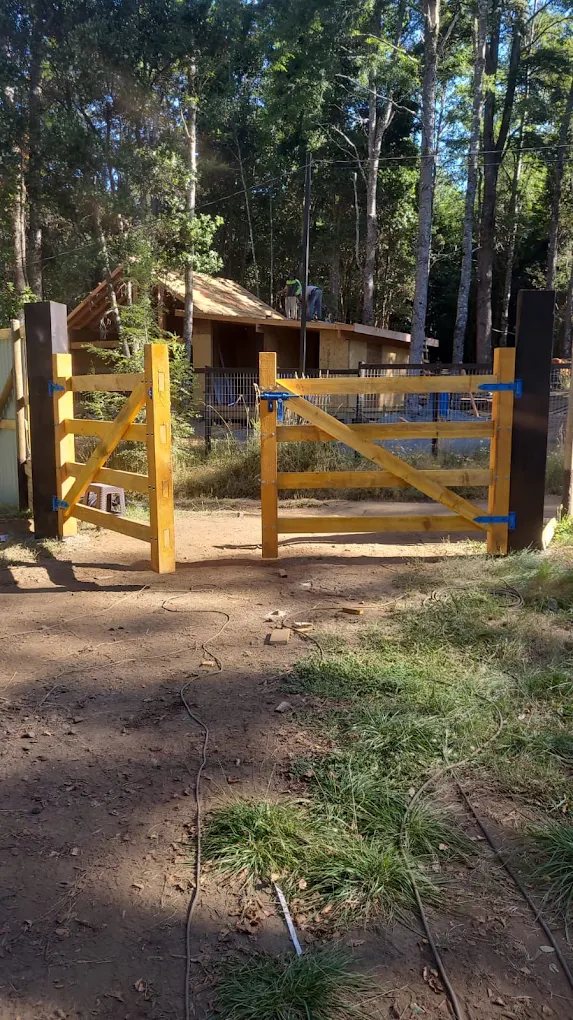Tranquera de madera amarilla en la entrada de una cabaña rodeada de árboles.