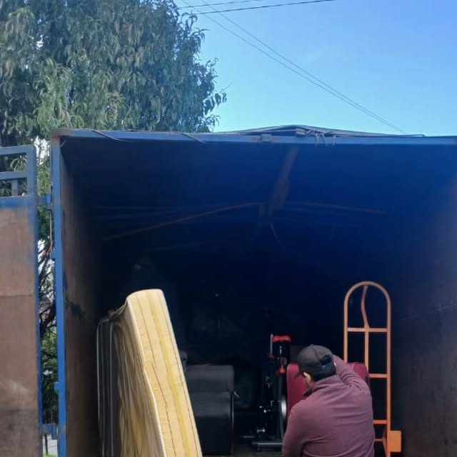 Interior del camión durante una carga, con un colchón envuelto y el carro de carga apoyado.